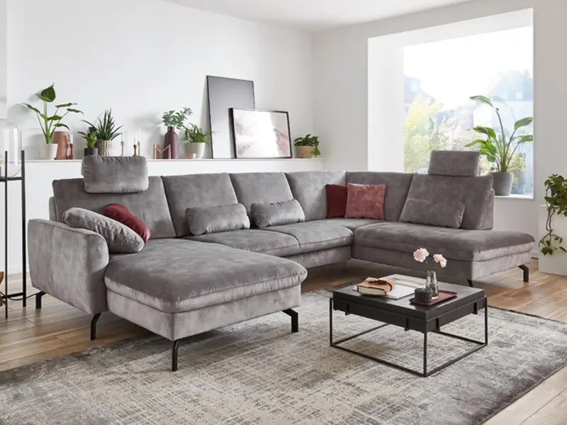 Großes graues Ecksofa mit Kissen in modernem Wohnzimmer mit Pflanzen und niedrigen Couchtischen.