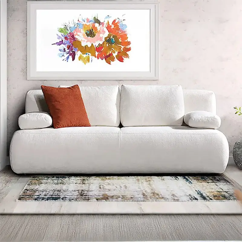 Weißes, modernes Sofa mit einem orangefarbenen Kissen vor einer Wand mit farbenfrohem Blumenbild und Teppich.